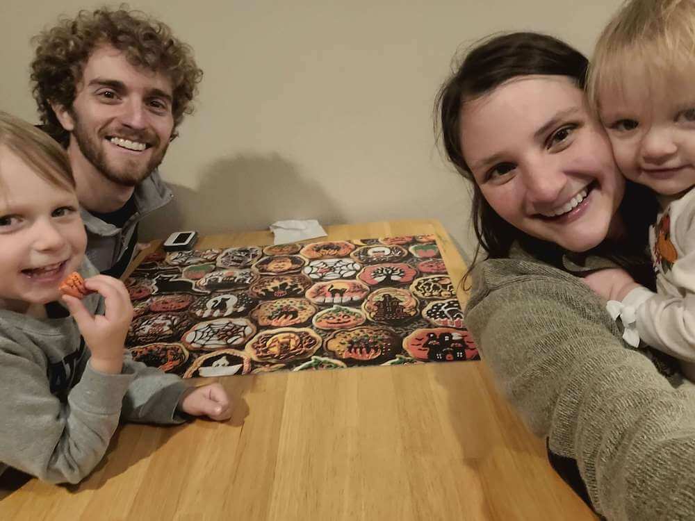 Man and woman with two children around a finished puzzle of halloween cookies