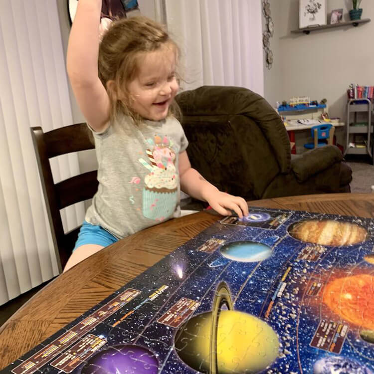 Excited little girl with a completed puzzle of the solar system