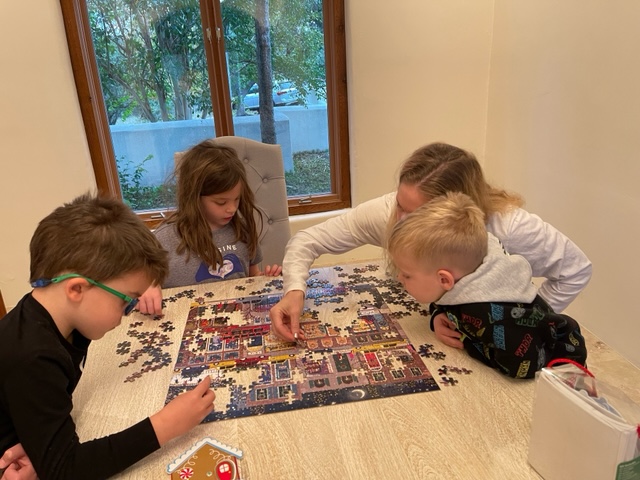 Woman and 3 children puzzling in front of a window