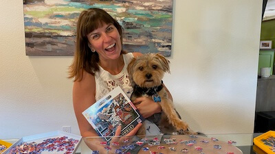 Woman holding dog and puzzle with puzzle pieces on table